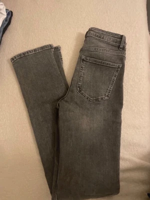 Grå  jeans från Zara - Säljer ett par grå skinny jeans från Zara med hög midja och klassisk femficksdesign. Jeansen har slitningar vid knäet och är gjorda i stretchig bomullsmix för skön passform. Perfekt för dig som gillar en smal siluett och coola detaljer.