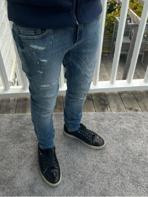 Blå jeans från Jack & Jones - Säljer ett par blå skinny jeans från Jack & Jones med slitna detaljer och klassisk femficksdesign. Jeansen har låg midja och är tillverkade i stretchig bomull för skön passform. Perfekt för dig som gillar en smal siluett och lite ruffig look.
