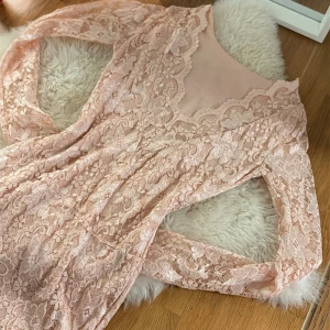 Ljusrosa spetsklänning från Lili - Supersöt ljusrosa spetsklänning från Lili med långärmad design och vacker blommig spets över hela klänningen. Klänningen har en feminin v-ringning och är figurnära med mjukt innerfoder. Perfekt för dig som vill ha en romantisk look. öppen baktill