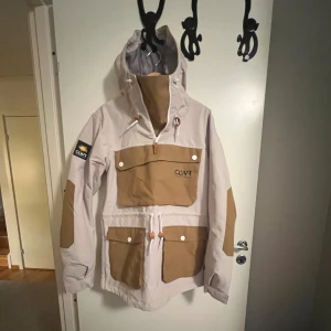 Beige och brun skidjacka CLWR S - Snygg skidjacka från CLWR i beige med bruna detaljer och stora fickor framtill. Jackan har huva, dragkedja och patch på ärmen. Knappt använd max 2 gngr i backen. 