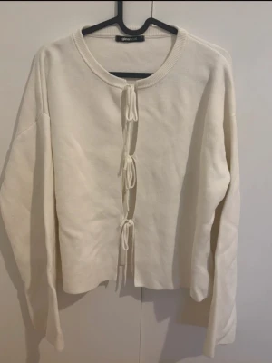 Vit kofta med snörning från Gina Tricot - Säljer en krämvit kofta från Gina Tricot med snygga snörningsdetaljer framtill. Koftan har lång ärm och är gjord i mjukt material som känns skönt mot huden. 