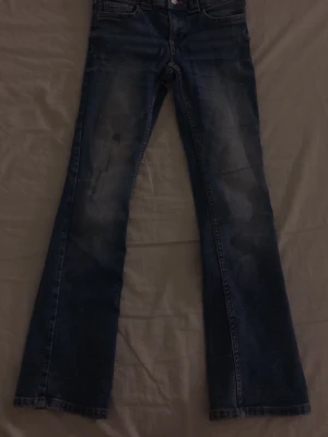 Blå bootcut jeans från Levi's - Säljer ett par klassiska blå jeans från Levi's med bootcut-snitt. Jeansen har en mörk tvätt med snygga slitningar framtill och fem fickor. Perfekt för dig som gillar retrovibbar och vill ha ett par jeans med lite extra attityd.