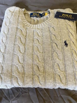 Ljusgrå  tröja Polo Ralph Lauren - Säljer en gråstickad tröja från Polo Ralph Lauren. Helt ny och aldrig använd. Storlek S. Klassisk och tidlös design som passar till allt.  Skickas snabbt 📦 Skriv vid frågor!