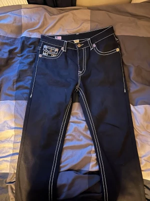 Svarta true religion - Ett par riktigt feta svarta true religion jeans med vita sömmar. Nästintill oanvända för dom är lite för stora för mig i storlek 34. Passar bra till alla outfits och perfekt för dig som vill sticka ut