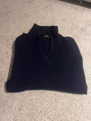 Mörkblå stickad half zip-tröja - Mörkblå stickad tröja från Blästa Henriqson med hög krage och half zip-dragkedja. Perfekt för kyliga dagar och enkel att styla med jeans eller chinos. Klassisk och tidlös design som funkar till det mesta.