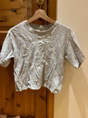 Croppad T-shirt - Ljus grå croppad T-shirt. Väl använd, något sliten i texten. Bild på slitage finns med. Storlek 164 från H&M. Djur och rökfritt hem.