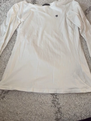 Vit långärmad topp från Marc O'Polo - Säljer en stilren vit långärmad topp från Marc O'Polo med rund hals och diskret broderad logga på bröstet. Toppen är gjord i mjuk bomull och har en normal passform som funkar till många olika looks.