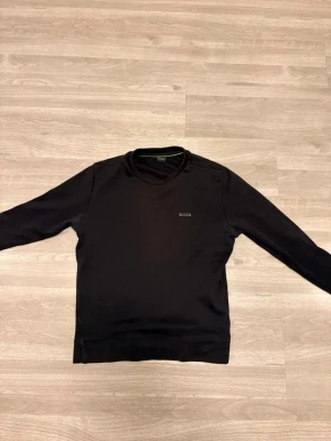 Svart långärmad tröja från BOSS - En stilren svart långärmad tröja från BOSS med diskret logga på bröstet. Tröjan har rund halsringning och är gjord i mjukt bomullsmaterial. Perfekt för en clean och enkel look.