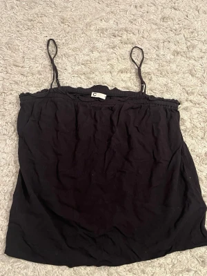 Svart linnetopp med tunna band - Säljer en svart linnetopp från Cubus i storlek XS. Toppen har tunna axelband och en lätt rynkad kant upptill för en söt touch. Materialet känns mjukt och luftigt, perfekt för varma dagar. Enkel och stilren design som är lätt att matcha.