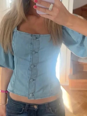 Ljusblå jeanskorsett med puffärm - Trendig ljusblå korsettopp i denim med puffiga trekvartsärmar och knappar framtill. Inga defekter 