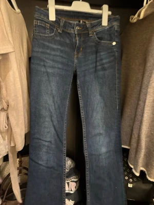 Blå bootcut jeans  - Säljer ett par blå bootcut jeans från Divided (H&M) i storlek 36. Jeansen har klassisk femficksmodell, snygga kontrastsömmar och broderade detaljer på bakfickorna. Materialet är jeans med en skön passform och lätt utsvängda ben.
