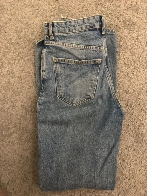 Blå jeans från g perfect jeans, storlek 34 - Säljer ett par klassiska blå jeans från g perfect jeans i storlek 34. Jeansen har en rak passform och är tillverkade i slitstarkt bomullsmaterial. De har en snygg sliten detalj med hål och fransar vid benslutet för en cool look.
