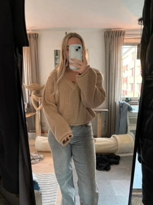 Beige croppad stickad tröja NA-KD - Supermysig croppad stickad tröja från NA-KD i beige. Tröjan har v-ringning, breda ärmar och en loose fit som ger en chill vibe. Perfekt att slänga på sig till jeans eller kjol för en snygg och avslappnad look.