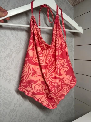 Rosa och röd halterneck linnetopp - Säljer en snygg halterneck linnetopp med rosa och rött abstrakt mönster. Toppen har tunna axelband som knyts i nacken och en lös, flowy passform. Perfekt för varma dagar och sommarens alla äventyr.
