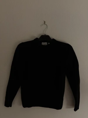 Svart stickad tröja från Bläck - Svart stickad tröja från Bläck i storlek S. Tröjan har rund hals och långa ärmar, perfekt för kyliga dagar. Materialet är en lyxig mix av 90% ull och 10% kashmir som gör den både mjuk och varm. Enkel och stilren design som funkar till många olika outfits.
