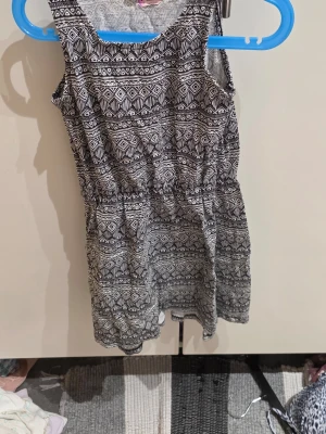 Svartvit mönstrad klänning KappAhl - Svartvit kortklänning från KappAhl i storlek 134. Klänningen har ett grafiskt mönster med elastisk midja och är ärmlös. Perfekt för varma dagar och enkel att matcha med sneakers eller sandaler.