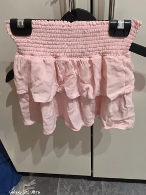 Ljusrosa volangkjol i viskos - Supersöt ljusrosa kortkjol från 157 med bred smock i midjan och dubbla volanger. Kjolen är gjord i mjuk och skön viskos som ger ett fint fall. Perfekt för dig som gillar romantisk och feminin stil. Passar dig som vill ha något gulligt och bekvämt.