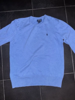 Ljusblå tröja från Polo Ralph Lauren - Snygg blå stickad tröja från Polo Ralph Lauren i storlek S/XS (xl barnstorlek).  Tröjan är i bra skick och passar dig som vill ha stilig, ”timeless” och minimalistisk stil
