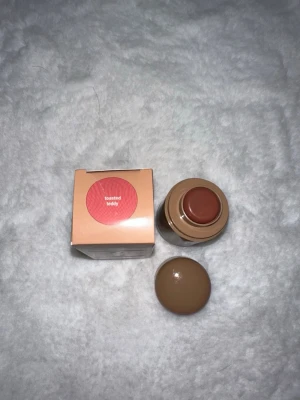 Rhode Pocket Blush Toasted Teddy - Rhode Pocket Blush i färgen Toasted Teddy, en krämrouge i stickformat med en varm, brunrosa ton. Kommer i en beige förpackning med rund lock och matchande kartong. Perfekt att ha med sig i väskan för snabba touch-ups.