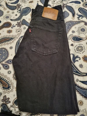 Svarta Levi's 501 jeans W29 L32 - Svarta Levi's 501 jeans med klassisk rak passform och femficksdesign. Jeansen har en snygg läderpatch bak i midjan och den ikoniska röda Levi's-taggen vid bakfickan. Tillverkade i slitstarkt bomullsmaterial och passar dig som gillar tidlös stil.