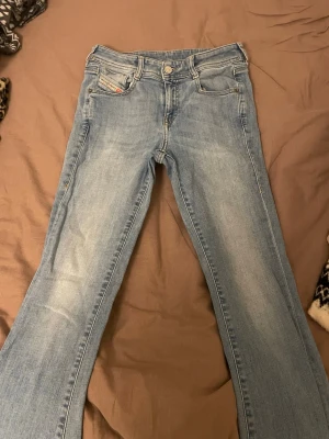 Ljusblå bootcut jeans från Diesel W25 - Säljer ett par ljusblå lågmidjade jeans från Diesel med klassisk femficksdesign och bootcut passform. Jeansen har snygga slitningar och en tydlig Diesel-logga på bakfickan. Tillverkade i mjukt denimtyg som sitter skönt hela dagen.
