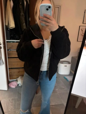 Svart teddyjacka från FILA med huva - Mysig svart teddyjacka från FILA i storlek M. Jackan har huva, dragkedja framtill med rund metallring och fickor med dragkedja. Perfekt för kyliga dagar och ger en chill vibe till din outfit.