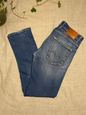 Replay Grover jeans blå denim - Säljer ett par Replay Grover jeans i klassisk blå denim med snygga slitningar och kontrastsömmar. Modellen har raka ben, fem fickor och läderpatch med Replay-logga bak i midjan. Perfekt för dig som gillar en tidlös jeansstil. 30/32