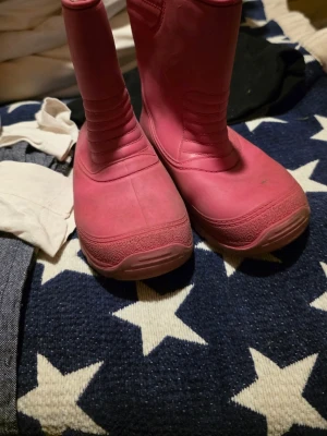 Rosa fodrade stövlar från Lejon  - Säljer ett par rosa stövlar från Lejon med grov mönstrad sula och mjukt grått foder på insidan. Stövlarna har en rund tå och är tillverkade i syntetmaterial, perfekta för kalla dagar. Snygga detaljer med sydda linjer och robust design.