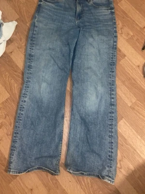 Blå wide jeans med raka ben - Säljer ett par blå jeans med breda, raka ben och klassisk femficksdesign. Jeansen har en ljus tvätt och är tillverkade i jeansmaterial. Passar dig som gillar avslappnad stil och vill ha ett par schyssta wide jeans till garderoben.