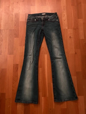 Bootcut jeans från Gina Tricot XS - Snygga blå lågmidjade bootcut jeans från Gina Tricot i storlek XS 14+. Jeansen har röda dekorativa sömmar, klassisk femficksdesign och cool broderad detalj på bakfickorna. Byxorna har en lätt tvättad look och dragkedja fram.