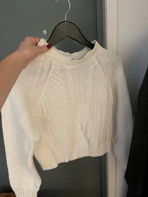 Vit stickad tröja med kabelmönster - Säljer en vit stickad tröja från NA-KD med snyggt kabelmönster och ribbade muddar vid hals, ärmslut och nederkant. Storlek xs, men är ganska liten i storleken. 