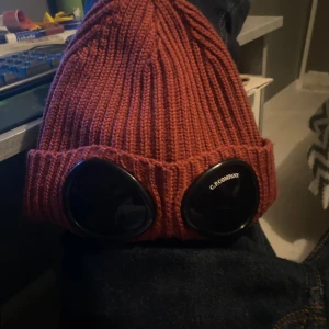 Röd/Vinröd  Goggle-mössa från C.P. Company - Säljer min C.P Company mössa då jag inte använder den längre. Det är väldigt bra skick med det är en liten spricka i glaset men annars är den bra. Har haft den i 1 vinter köpte för 1499kr och säljer för 800kr 
