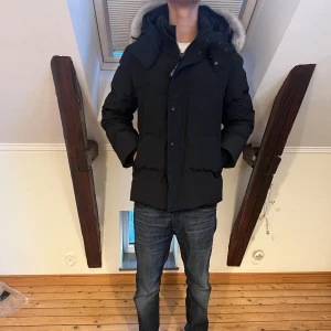 Svart dunjacka från Canada Goose black label - Säljer en svart dunjacka från Canada Goose med fluffig päls runt huvan. Jackan har dragkedja, knappar och flera fickor. Klassisk patch på ärmen och riktigt varm stoppning. Perfekt för kalla dagar och snygg passform. Påse följer med.