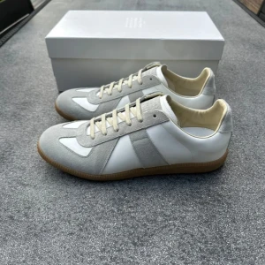 Maison Margiela sneakers vit/grå - Maison Margiela sneakers i vit och ljusgrå färg med klassisk design. Ovandel i skinn och mocka, beige innersula och gummisula med mönster. Rund tå och snörning framtill. Perfekt för dig som gillar stilrena och trendiga sneakers.