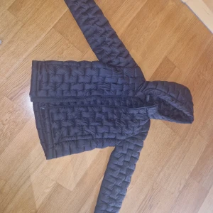 Svart dunjacka från Everest med huva - Svart dunjacka från Everest med quiltad design och huva. Jackan har dragkedja framtill och är lätt vadderad, perfekt för kyliga dagar. Enkel och stilren modell som funkar till det mesta. Passar dig som gillar en klassisk look.