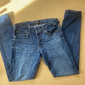 Blå jeans från Jack & Jones, strl 30/32 - Snygga blå jeans från Jack & Jones i modellen Glenn. Klassisk femficksdesign med kontrastsömmar och knappstängning. Jeansen har en smal passform och är tillverkade i mjukt denimtyg som sitter skönt hela dagen.