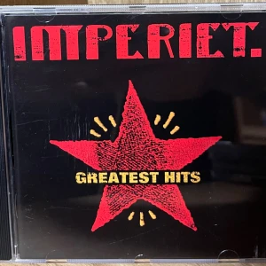 Imperiet - Greatest Hits CD - Samling med Imperiets största hits! Perfekt för dig som gillar svensk rock med attityd och energi. Omslaget har en ikonisk röd stjärna och låtlistan bjuder på klassiker som 'C.C. Cowboys', 'Var e vargen' och 'Kickar'. Ett måste för musikälskare och nostalgiker.