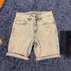 Ljusblå jeansshorts från Kappahl - Snygga ljusblå jeansshorts från Kappahl i klassisk femficksmodell. Shorts med upprullade benslut, bälteshällor och dragkedja med knapp. Perfekta för varma dagar och enkel att matcha med allt.