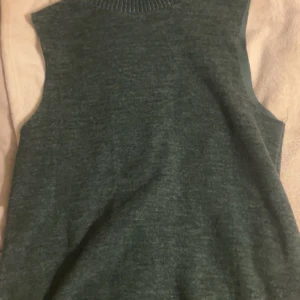 Mörkgrön stickad ärmlös topp - Mysig mörkgrön stickad topp med rund halsringning och ärmlös design. Perfekt att styla med skjorta under eller som den är för en enkel och clean look. Tidlös modell som funkar året runt.