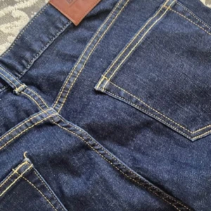 Mörkblå jeansbyxor W30 L32 - Snygga mörkblå jeansbyxor med klassisk rak passform och kontrasterande gula sömmar. Byxorna är tillverkade i 95% bomull och 1% elastan för lite stretch. Perfekta för dig som gillar en tidlös jeanslook.