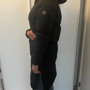 Svart lång dunjacka Cross Sportswear - Cross Sportswear, svart halvlång dunkappa med luva, stl small. Gott skick.