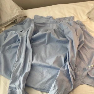 Ljusblå slim fit skjorta Polo Ralph Lauren - Säljer en ljusblå skjorta från Polo Ralph Lauren i slim fit-modell. Skjortan har klassisk krage, långa ärmar med knappar vid manschetterna och den ikoniska broderade loggan på bröstet. Tillverkad i mjuk bomull för en clean och fräsch look.