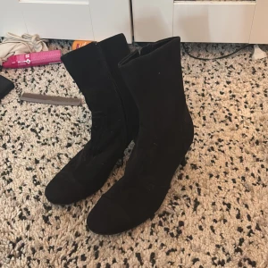 Svarta stövletter med klack - Snygga svarta stövletter i mocka-look med spetsig tå och smal klack. Skorna har dragkedja på insidan för enkel påtagning och en stilren design som passar till många outfits. Perfekta för dig som vill ha en klassisk men trendig sko.