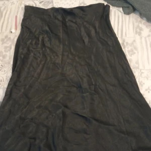 Svart långkjol från Weekday - Säljer en svart långkjol från Weekday i storlek 44. Kjolen har en stilren och flowy passform med lätt glansigt tyg som ger en snygg look. Perfekt för dig som gillar minimalistisk stil och vill ha en kjol som känns både trendig och enkel att matcha.