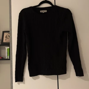 Svart stickad tröja Basic You S - Svart stickad tröja från Basic You i ekologisk bomull. Tröjan har rund halsringning, ribbade muddar och lång ärm. Perfekt för lager-på-lager och enkel att matcha med allt. Snyggt diskret mönster i stickningen för extra stilpoäng.