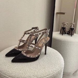 Valentino Rockstud pumps svart/beige - Säljer ett par ikoniska Valentino Rockstud pumps med spetsig tå och hög klack. Skorna är svarta i lackat skinn med beige remmar dekorerade med guldiga nitar. Snygg design med flera remmar och spänne runt vristen. Perfekta för dig som vill sticka ut.