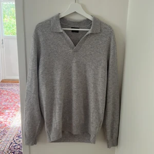 Grå ulltröja med krage från Massimo Dutti - Säljer en stilren grå långärmad tröja från Massimo Dutti i extrafin ull. Tröjan har en klassisk krage med v-ringning och är perfekt för dig som gillar en clean och tidlös look. Är i nyskick eftersom jag ej har använt den.