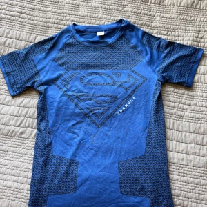 Blå Superman t-shirt från YoungLA - Blå t-shirt från YoungLA med stort Superman-tryck på bröstet och coola svarta mönsterdetaljer på ärmar och sidor. Kortärmad och tillverkad i ett stretchigt material som passar perfekt till träning eller chill. Snygg passform och sportig vibe.