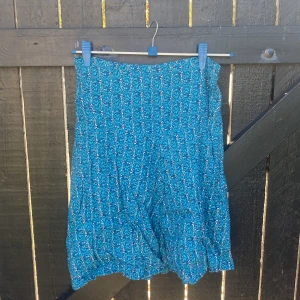 Blommig blå kjol från Noa Noa XS - Supersöt blå kjol från Noa Noa i storlek XS med blommigt mönster i vitt och rosa. Kjolen är kort, har en lätt utställd form och är tillverkad i ett tunt, skönt bomullstyg. Perfekt för varma dagar och ger en fräsch och somrig vibe.