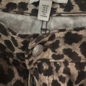 Leopardmönstrade byxor i jeanstyg  - Säljer ett par snygga byxor med leopardmönster. Byxorna har klassisk femficksdesign, raka ben och knäppning fram. Perfekta för dig som vill sticka ut med ett djurmönstrat statement-plagg.